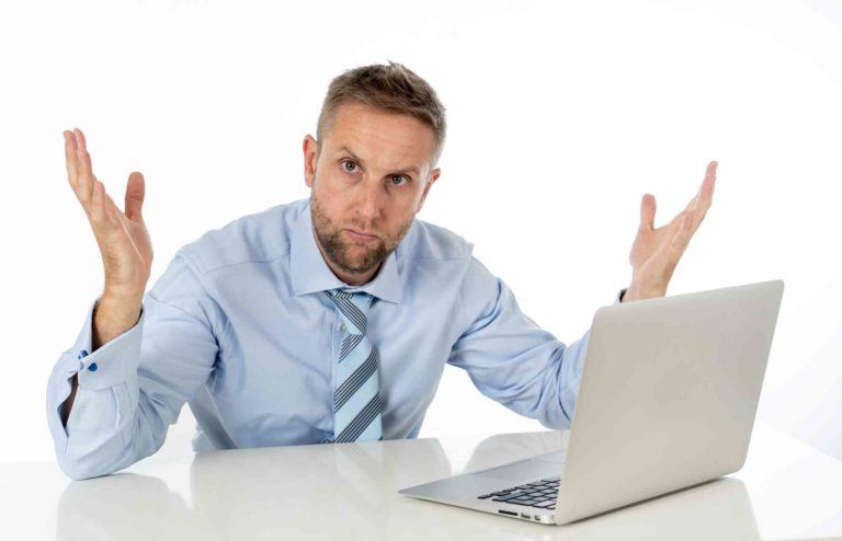 Mann sitzt fragend beim Tisch mit Computer